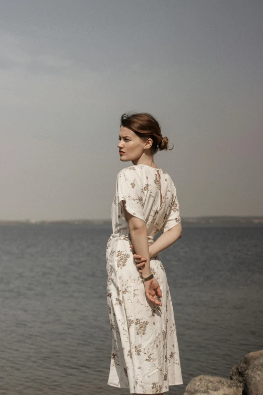 a woman in a white dress is standing by the water