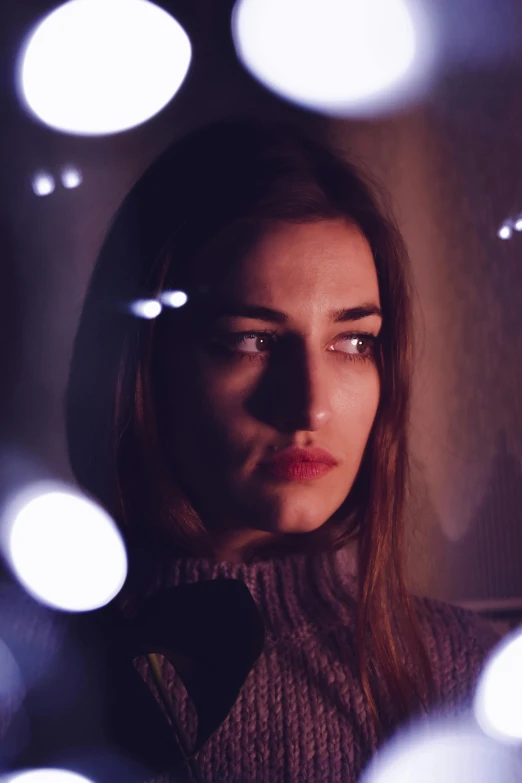 a young woman looks at the camera while lights shine on her