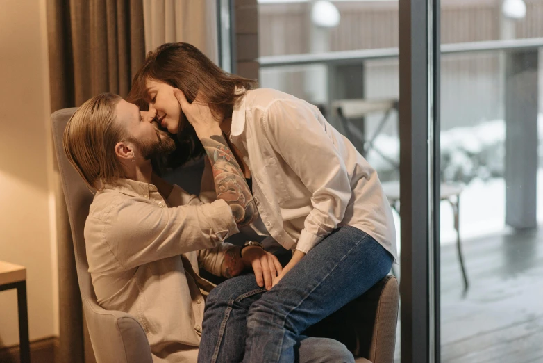 two men are sitting and sharing a kiss in front of a window