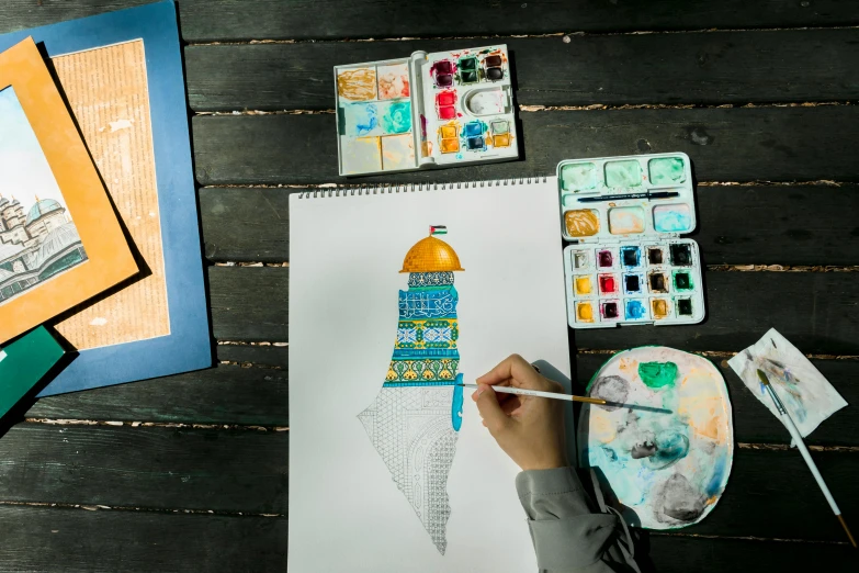 person using brush marker on a paper with watercolors and painting supplies around it