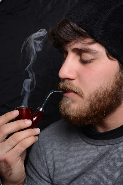 a man smoking with his eyes closed while holding a pipe