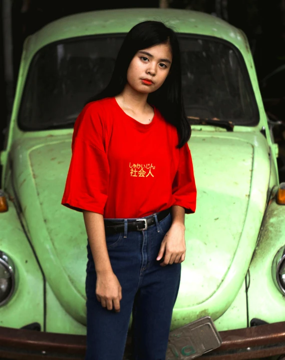 a girl wearing a red shirt is standing next to a green beetle