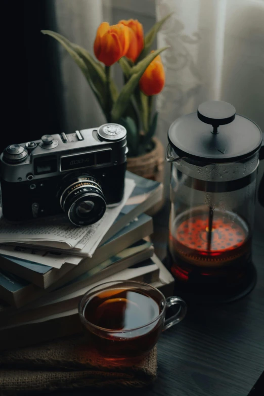 an orange tulip in a vase next to some coffee and books