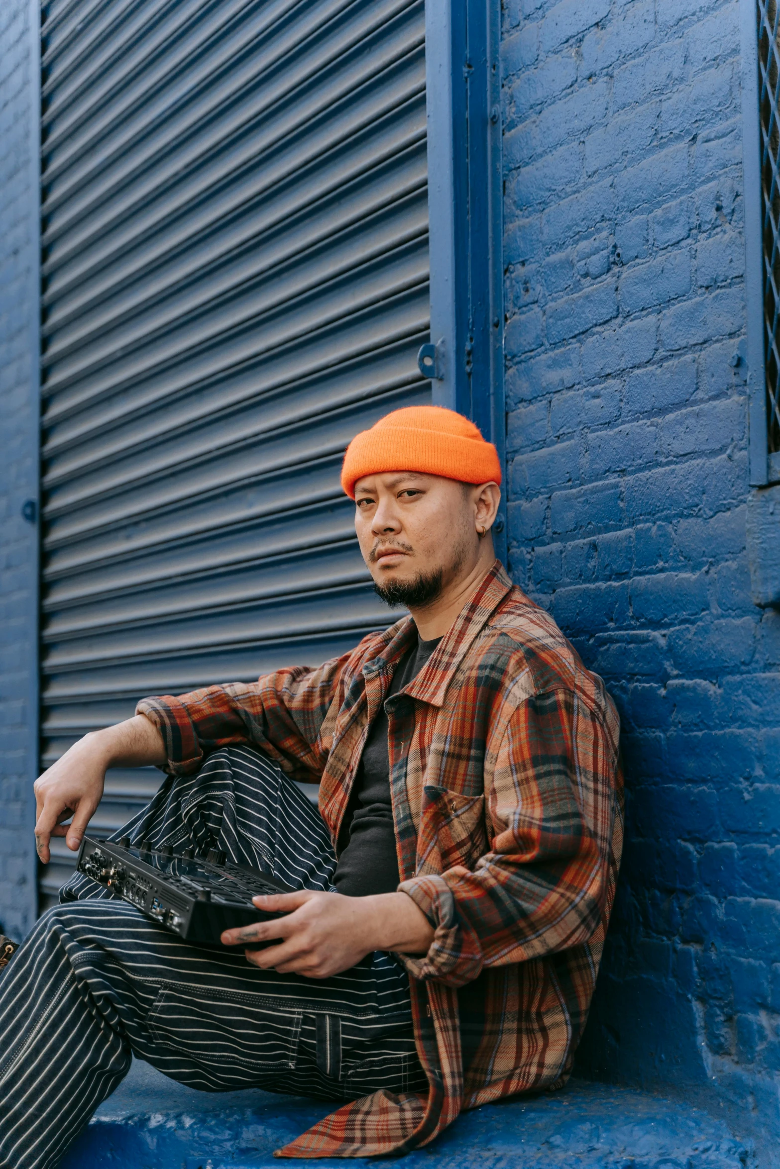 a man with a knitted orange beanie sitting on the corner of a building