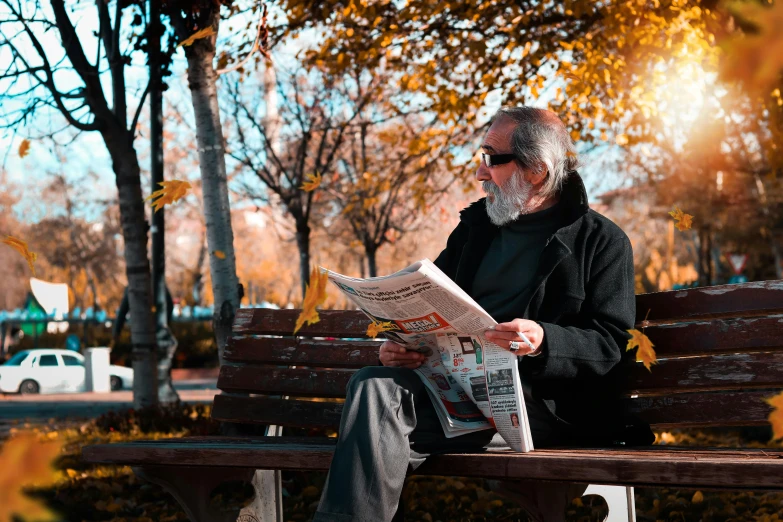 a man sitting on a bench while reading a paper
