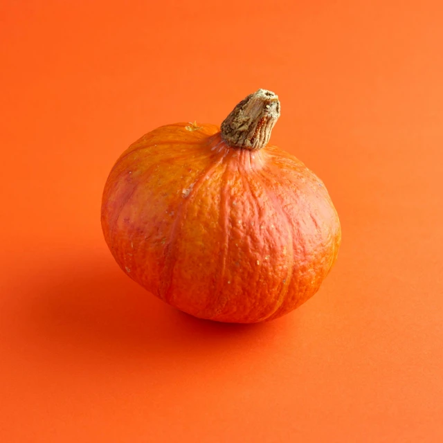 an orange pumpkin on an orange background with an ugly looking face