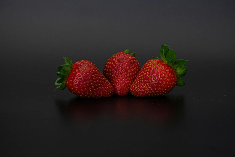 three strawberries stacked together on black background
