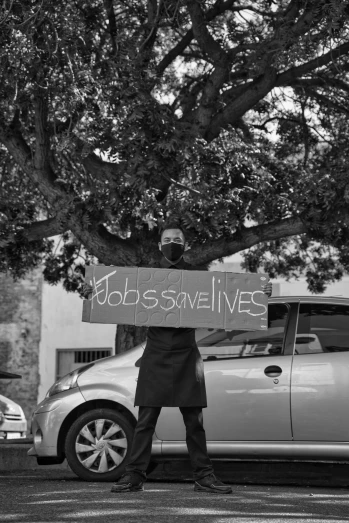 a man holding up a sign in front of his car