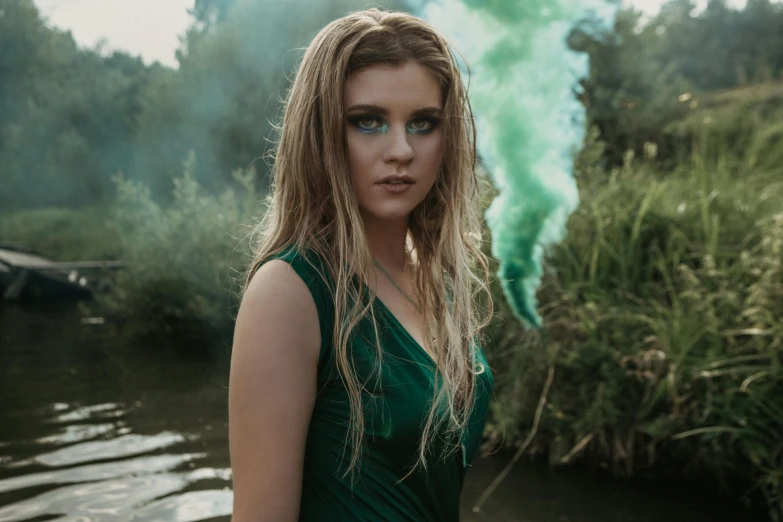 a beautiful young woman in green dress standing by water