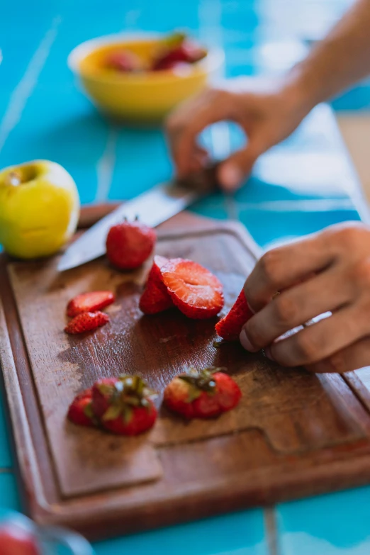 someone chopping up some strawberries on a board