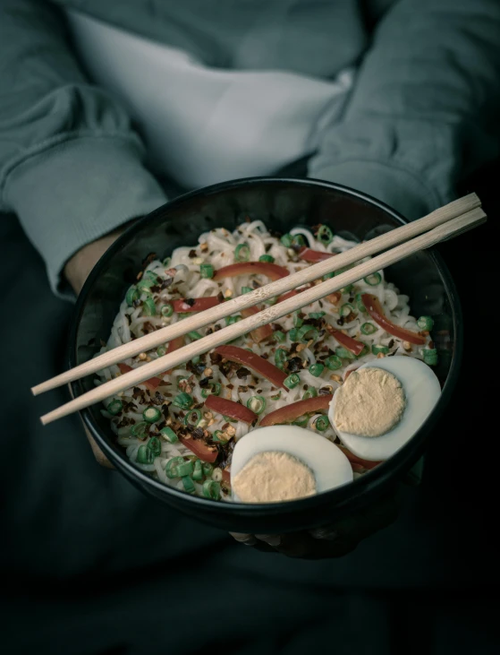 a person holding up an egg and rice bowl with chopsticks