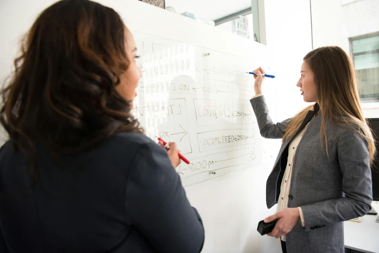 a woman points at the screen while another woman holds a pencil