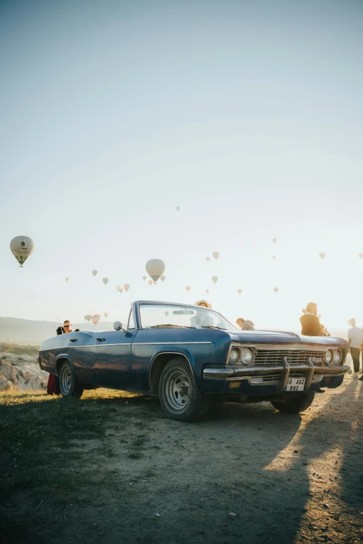 people are standing around an old car and some  air balloons