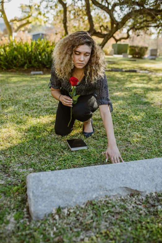 a woman placing a red rose in the grave