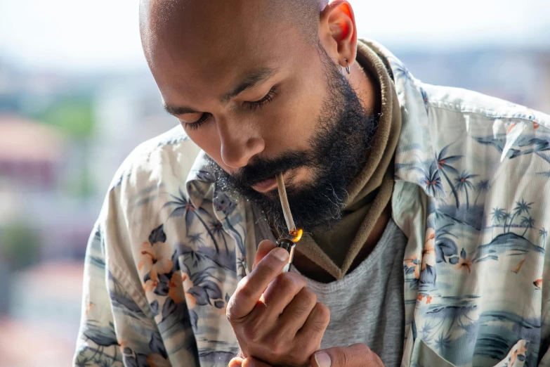a bearded man wearing a tropical shirt holding a cigarette in his mouth