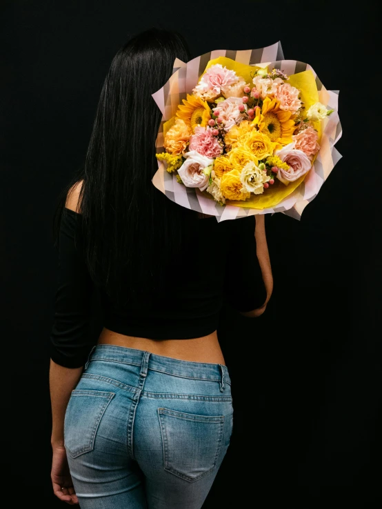 a woman with long hair and wearing a black top holding a bunch of flowers