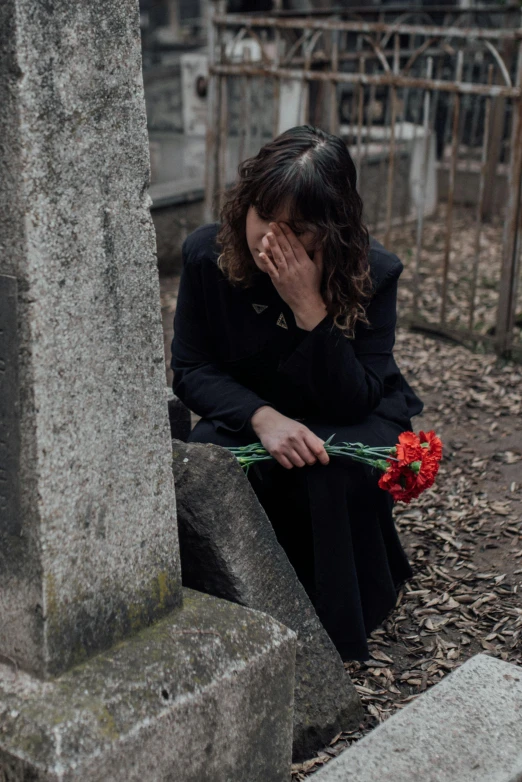 a woman kneeling in front of a grave holding flowers