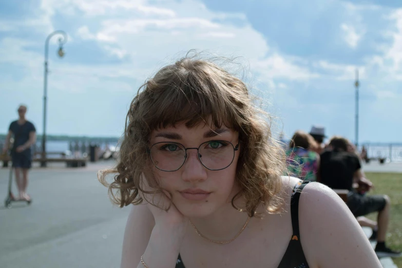 woman in glasses poses near several people near water