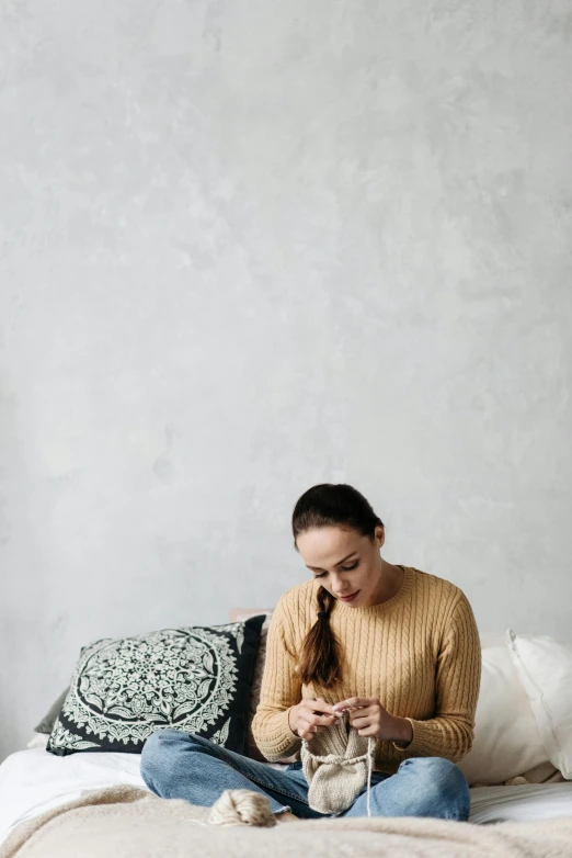 a woman sitting on the bed is holding a pair of scissors