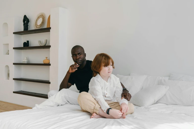 a man sitting next to a little girl on top of a bed