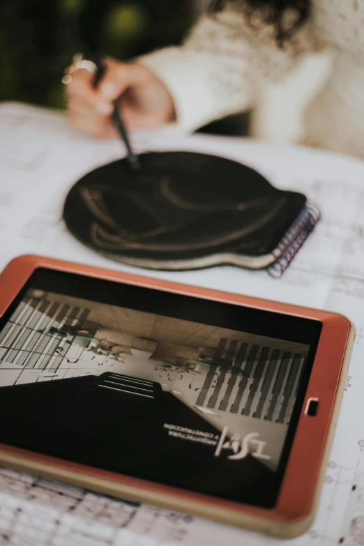 a tablet on a table near a person writing on the pad