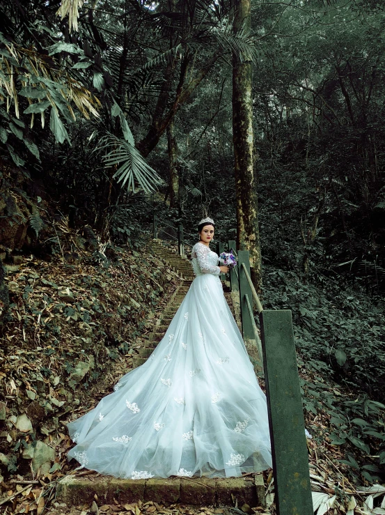 a bride in a wedding gown is standing on a bridge and looking at soing while the camera woman stands behind her