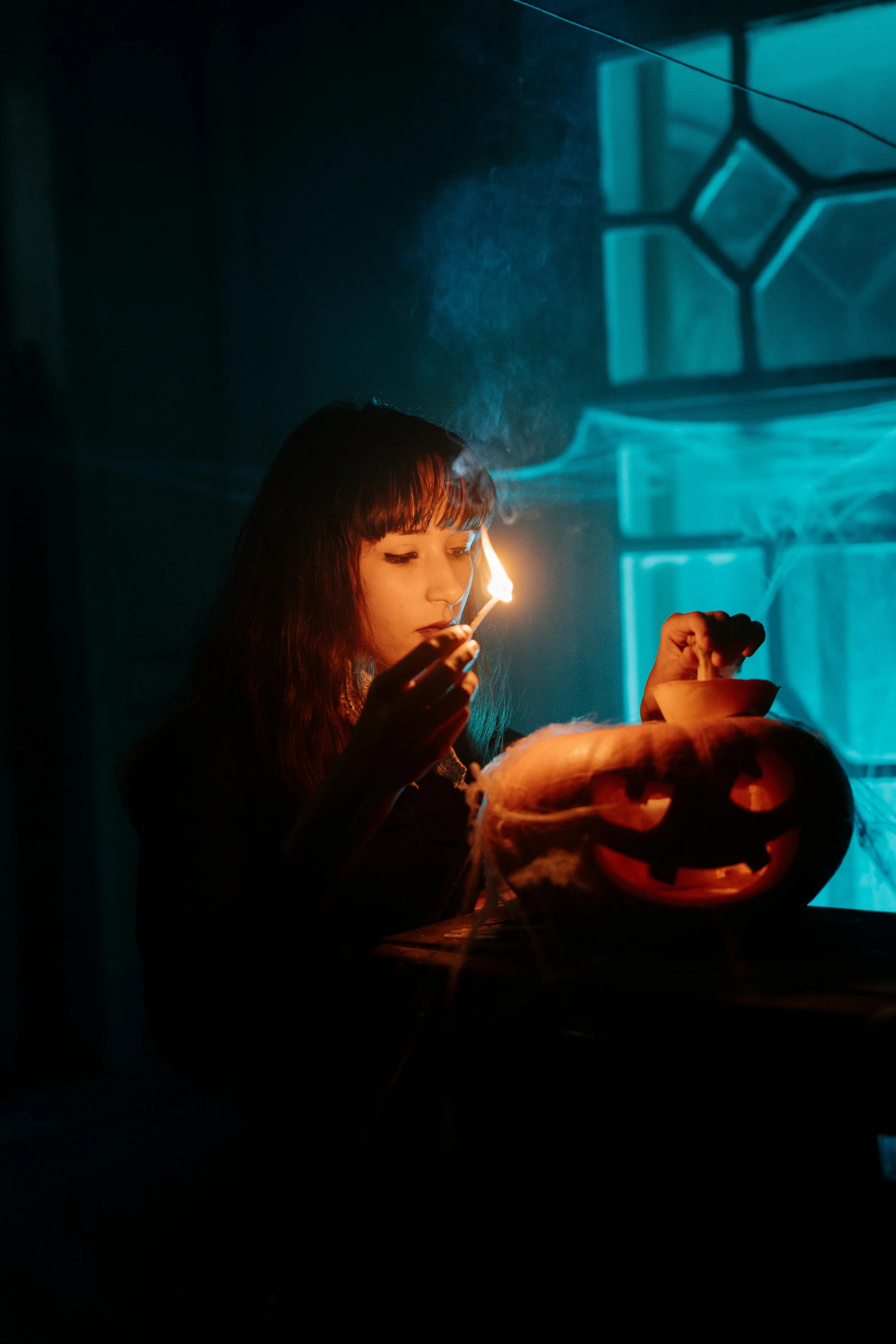 a girl lights her candle as she sits in front of an orange lit pumpkin