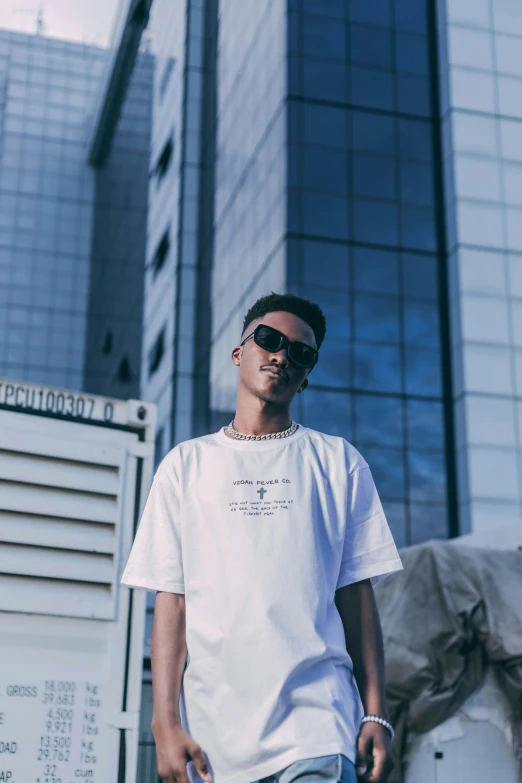 a man wearing a white t - shirt and jeans standing in front of a building