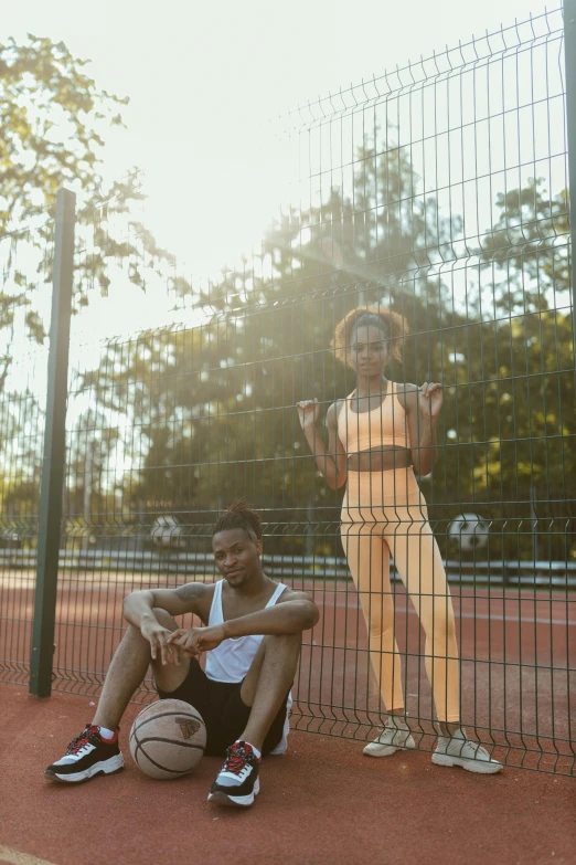 the man sits on a basketball as he talks to the lady on a court