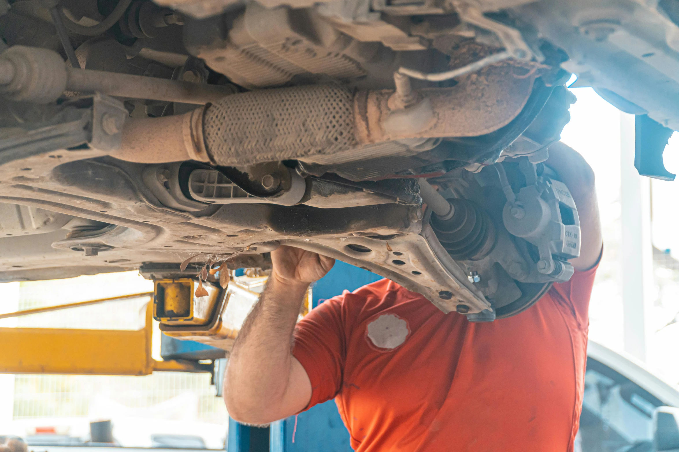 man with an orange t - shirt underneath a vehicle