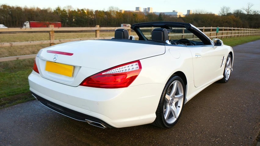 a mercedes benz roadster sits parked in front of a fence