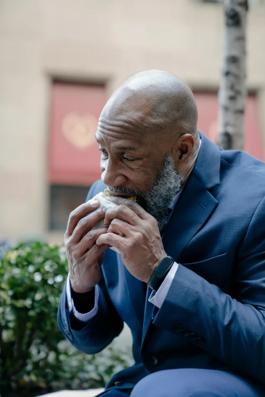 an older man in a blue suit is sitting outside and eating