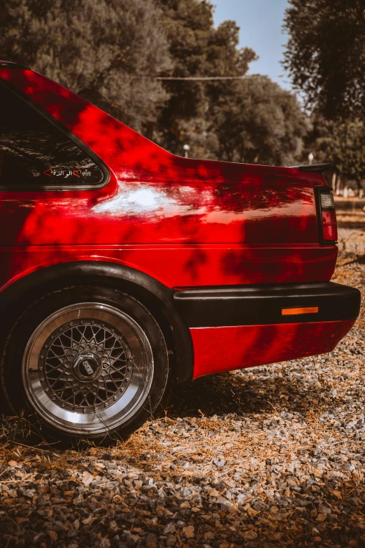 a red car parked in the dirt and leaves