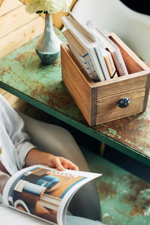 a person's hand holding a magazine next to a table with flowers