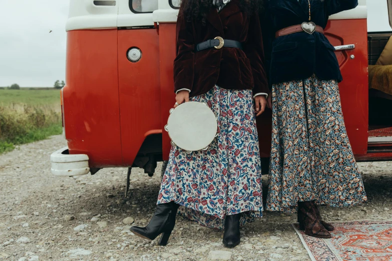 two people wearing dress and sunglasses standing in front of an old bus