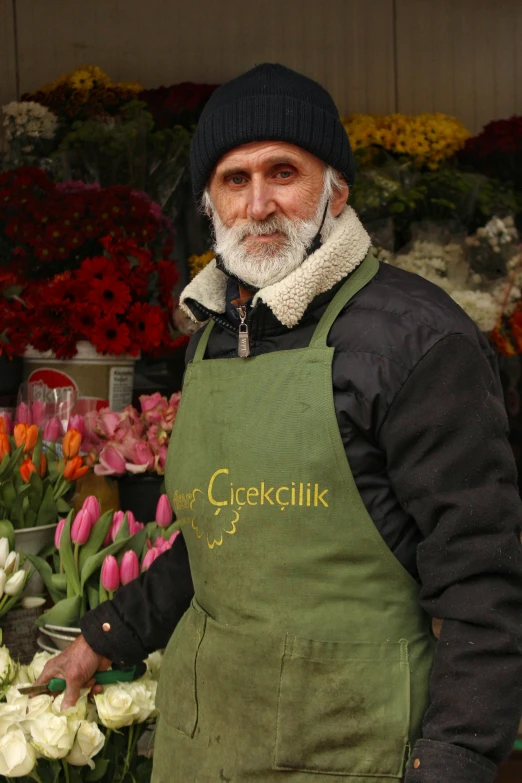 a man in an apron standing with flowers behind him