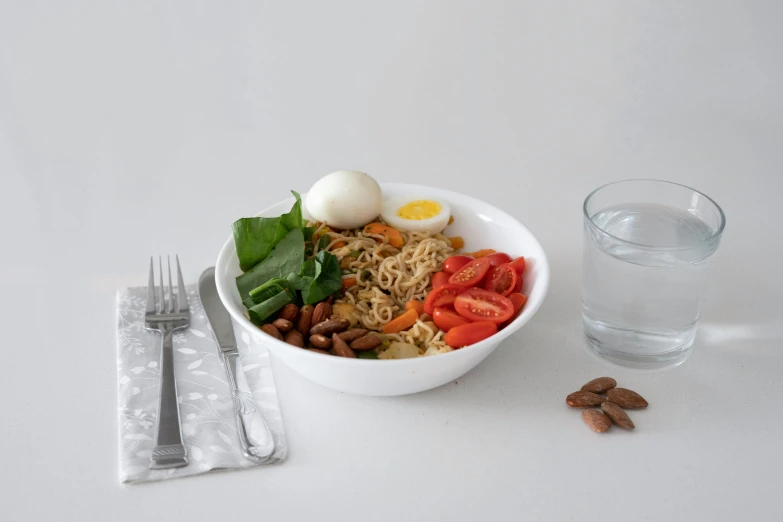 a white bowl filled with pasta and veggies next to a glass of water