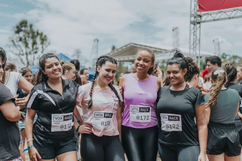 three women in muddy black wetsuits are standing near a crowd