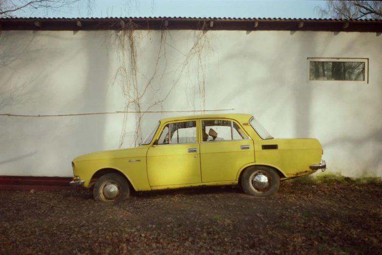 an old yellow car parked in front of a white building