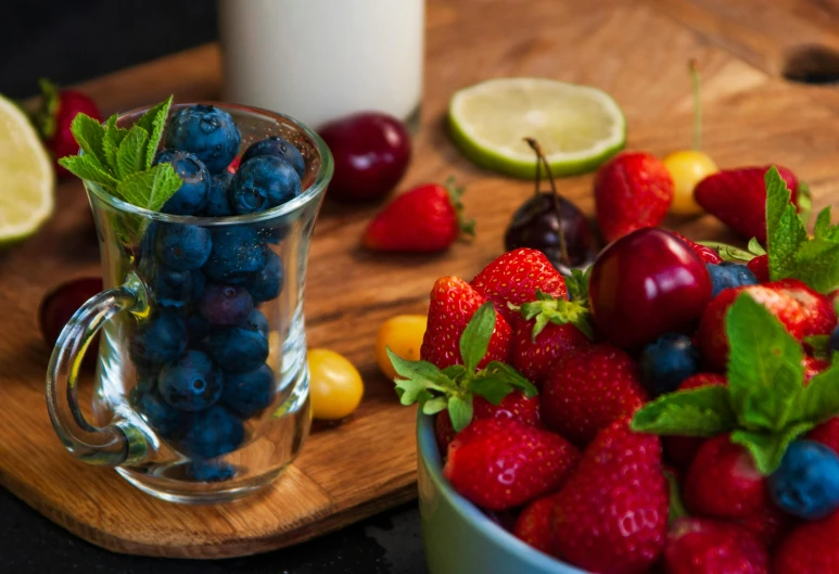 a bowl of berries, lemons, and blueberries on a  board