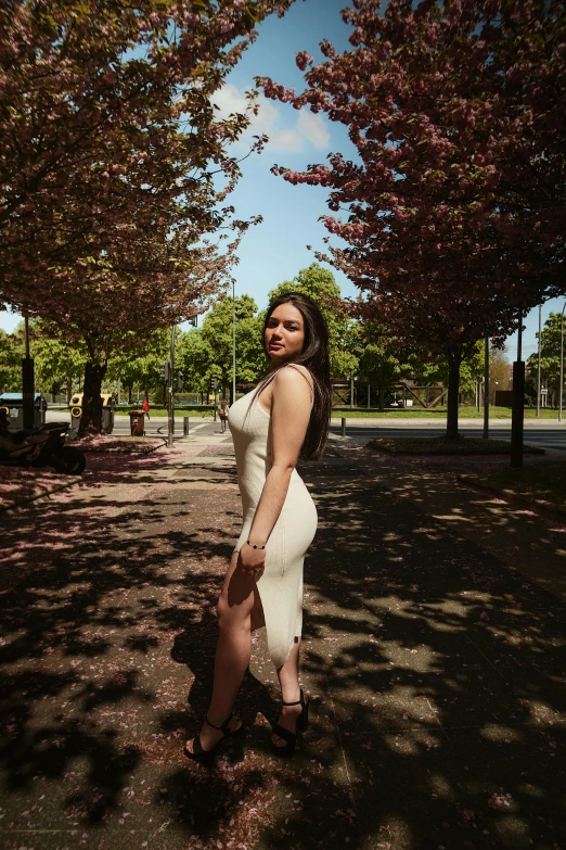 a pregnant woman posing on some dirt with pink trees around her