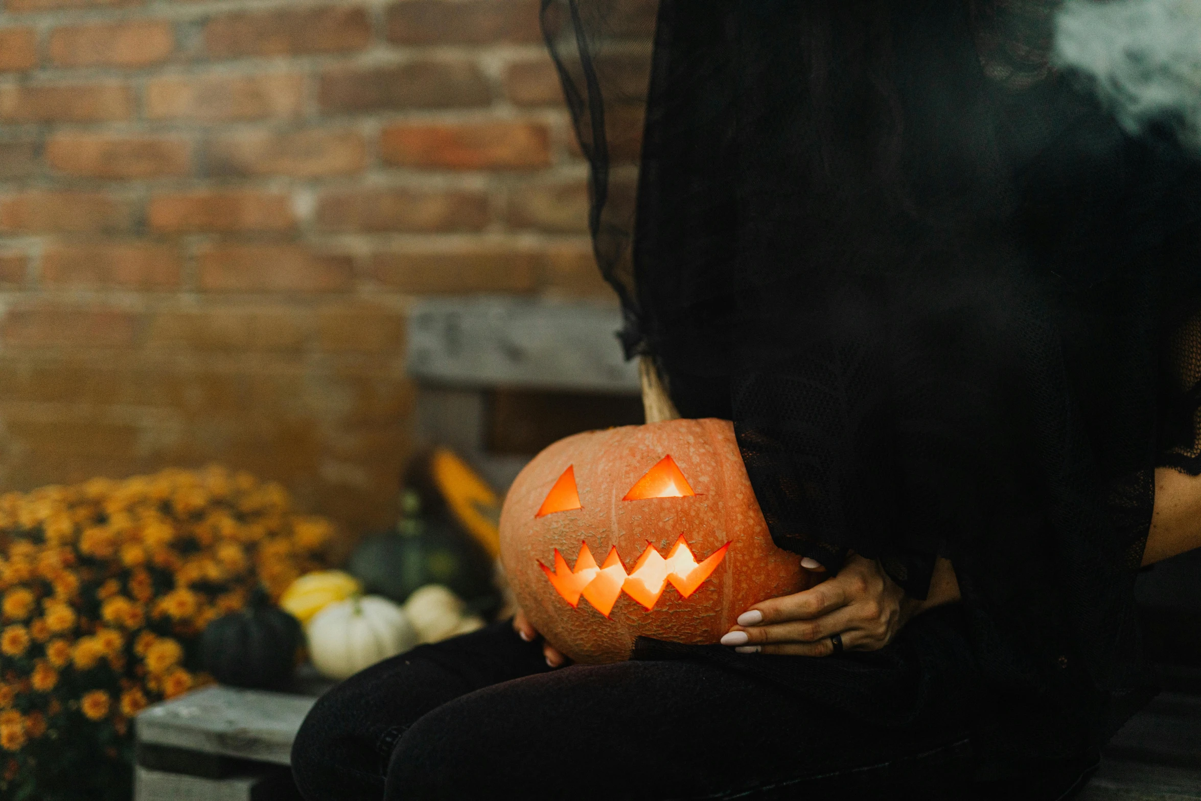 someone holds up a carved pumpkin as they sit in front of a bunch of flowers