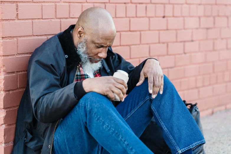 a man sitting against a brick wall looking at his cell phone