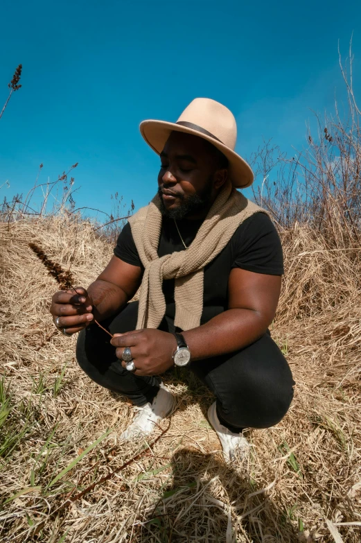 a man with a straw hat sits on the ground, holding soing