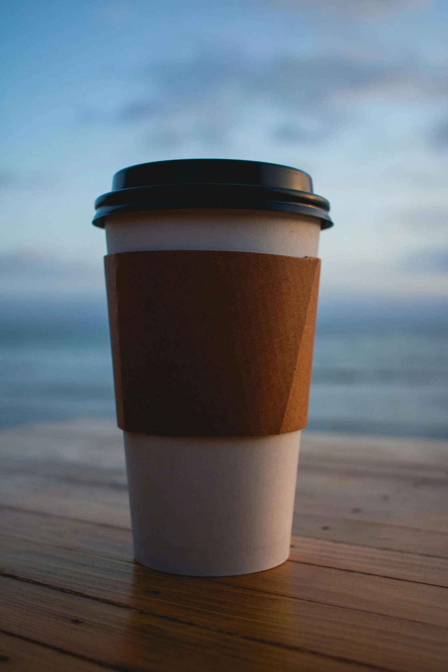 a coffee cup is standing on the deck near the ocean