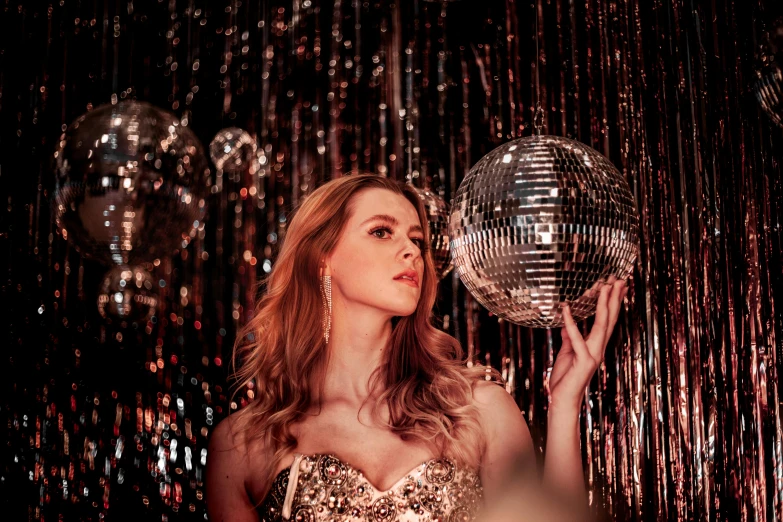 a woman wearing gold is holding a disco ball