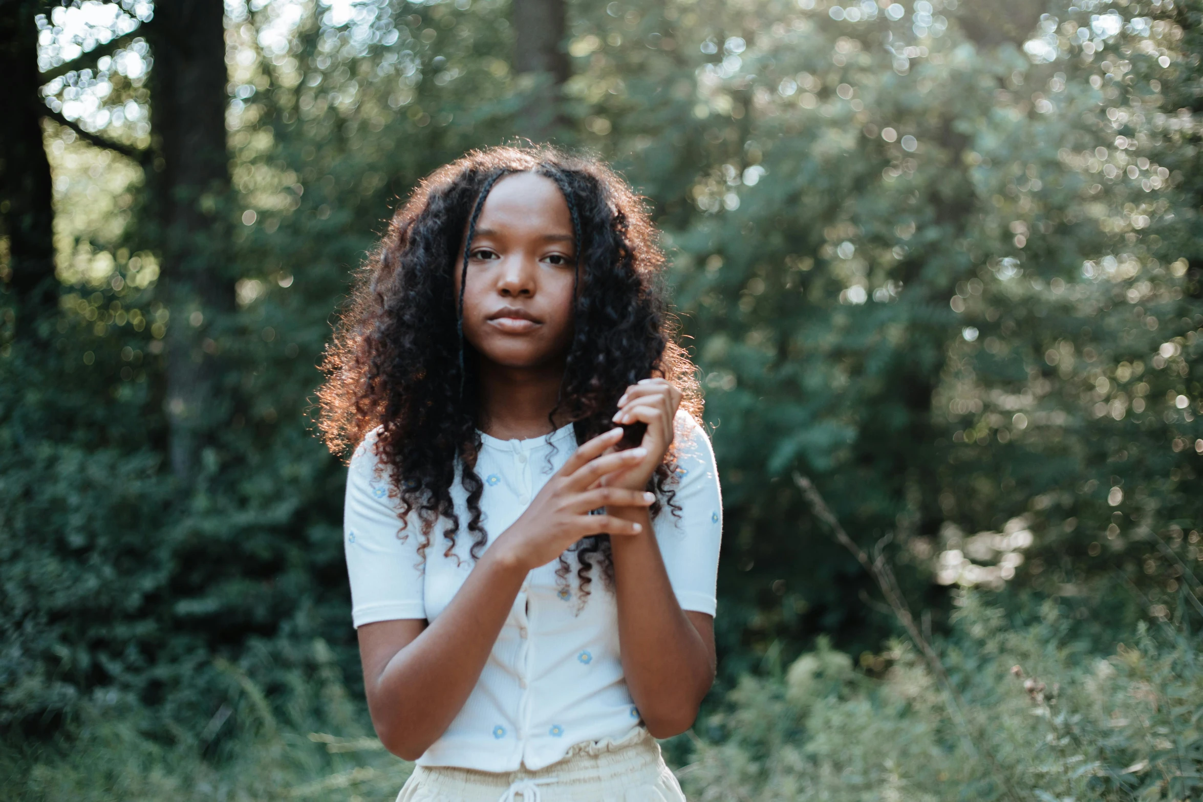 a young woman stands in a forest holding an object