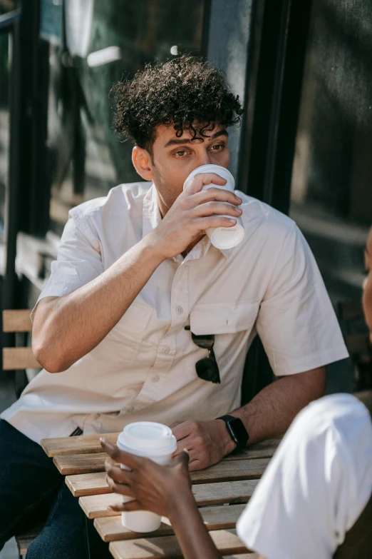 a man sitting on top of a bench drinking from a paper cup