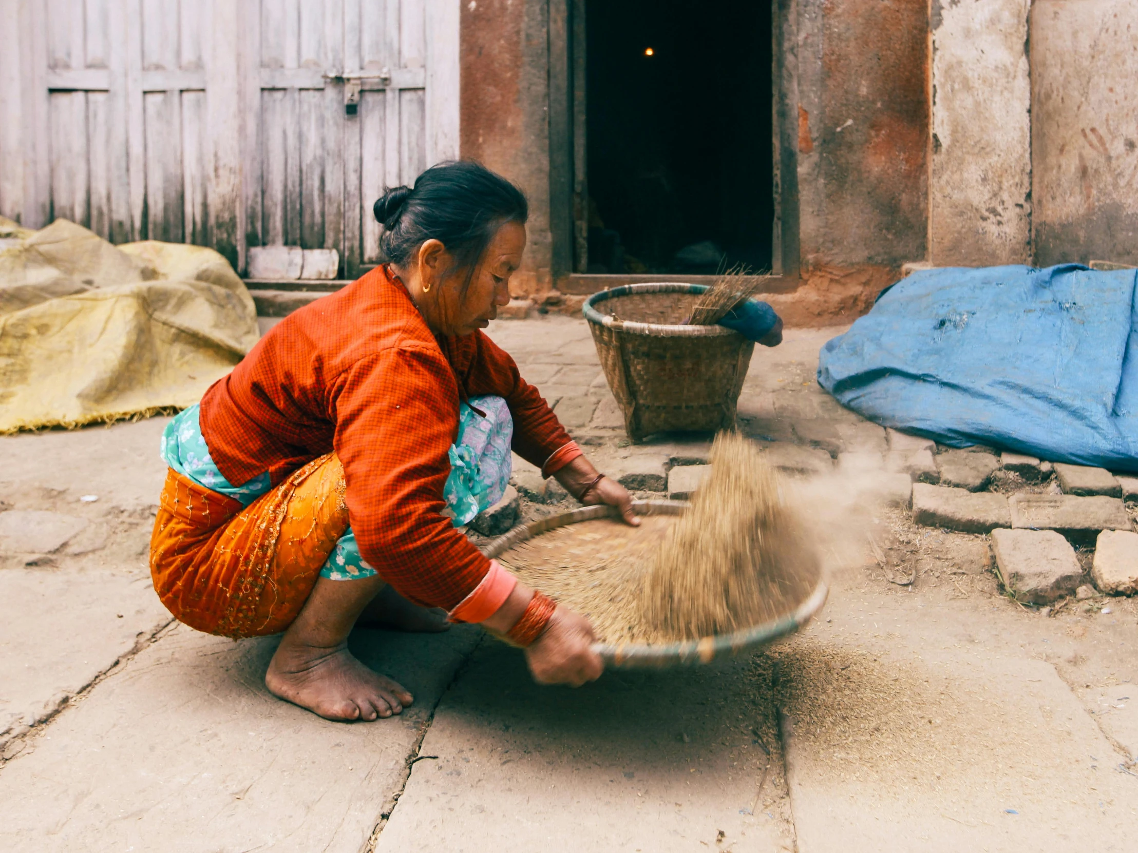 a woman in a colorful shirt sitting on a concrete ground next to a basket