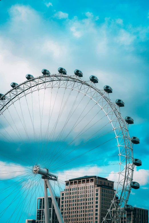 a ferris wheel sitting in front of a building with the sky filled with clouds